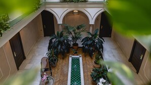 Ein Innenhof mit einem zentralen Wasserspiel, umgeben von Topfpflanzen und Sitzbereichen.