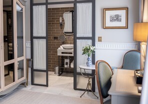A modern bathroom with a large mirror, a sink, and a toilet. There is a small table with a vase of flowers and a chair. - Hotel Gravina 51 (Seville)