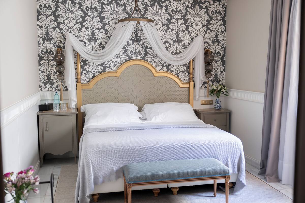 A neatly made bed with a white and blue striped bedspread, a wooden headboard, and a bench at the foot of the bed.