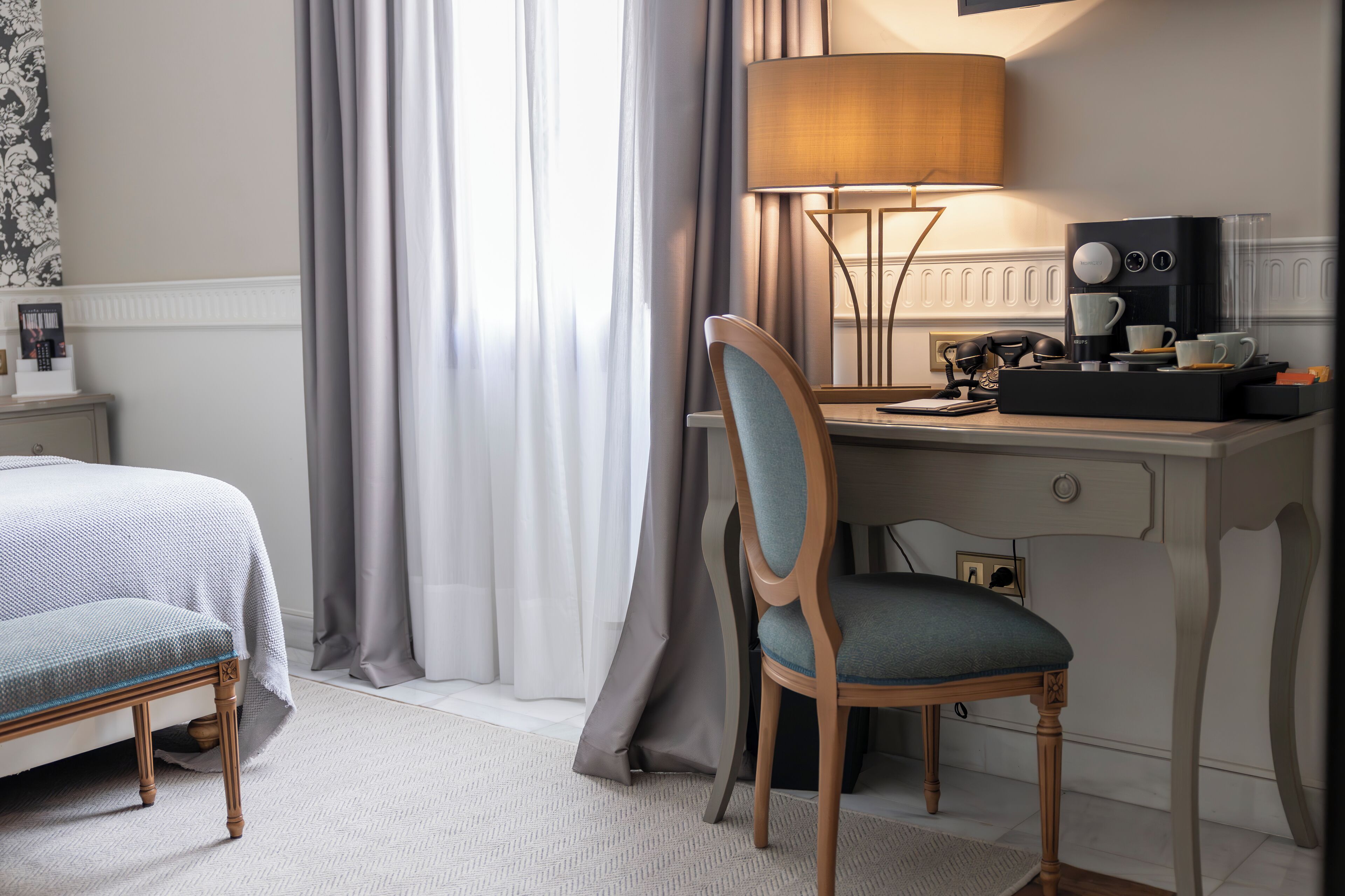 Habitación de hotel con cama, escritorio con lámpara, silla y cafetera.