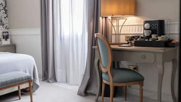 Habitación de hotel con cama, escritorio con lámpara, silla y cafetera.