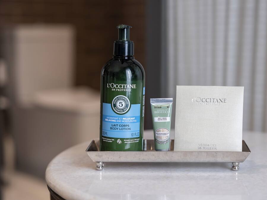 En badrumsmöbel med en flaska L'OCCITANE-kroppslotion, ett tub med kroppskräm och en liten låda för toalettartiklar.