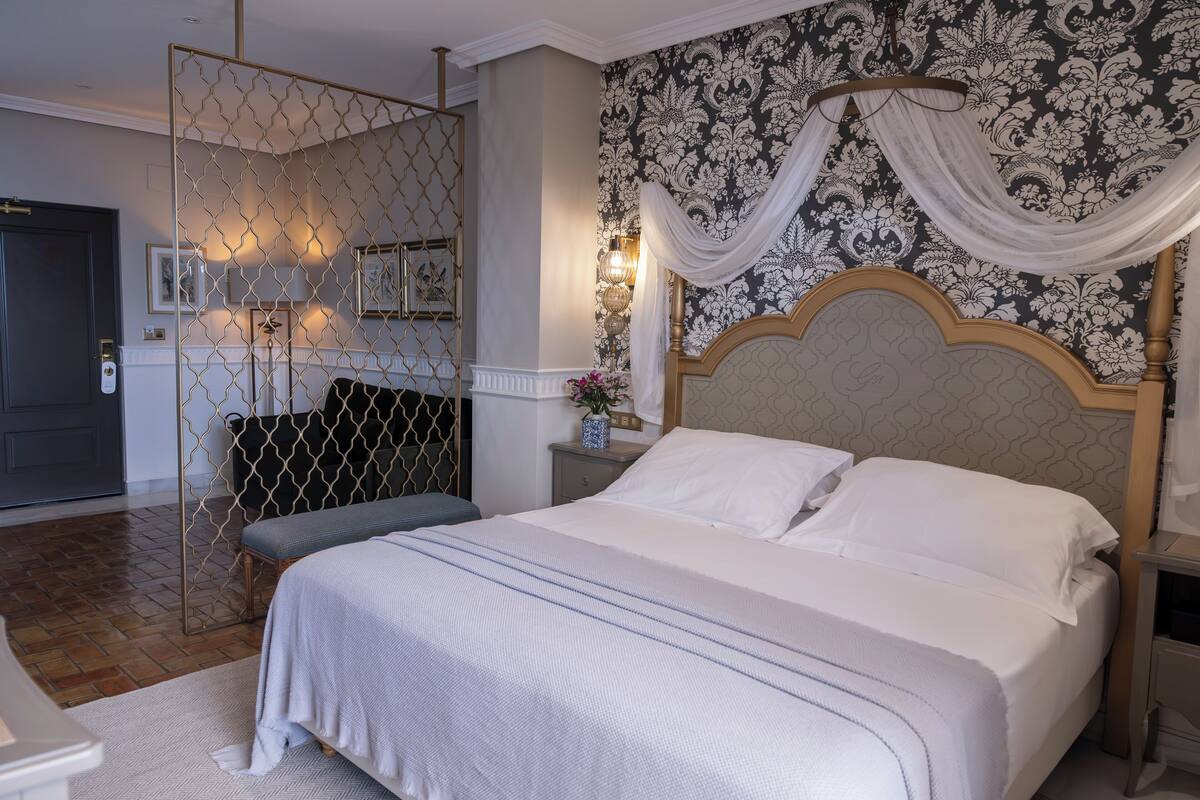 A neatly made bed with white linens, a headboard with a decorative design, and a wall with a patterned wallpaper.