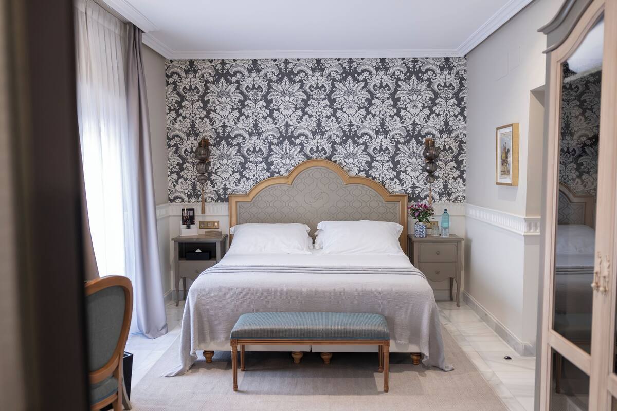 A neatly arranged bedroom with a large bed, bedside tables, a bench, and a wardrobe.