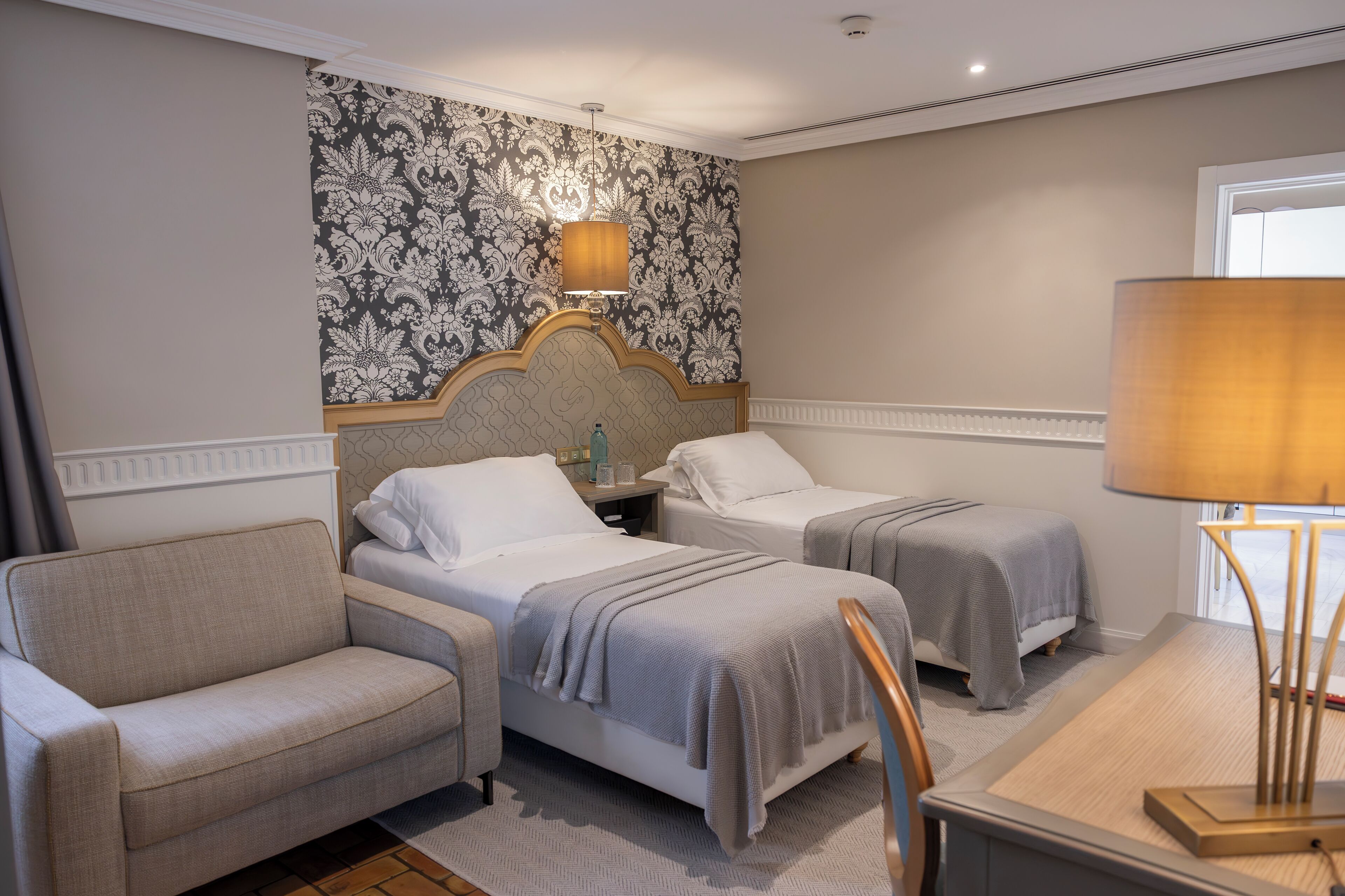 A hotel room with two beds, a sofa, a table, and a lamp.