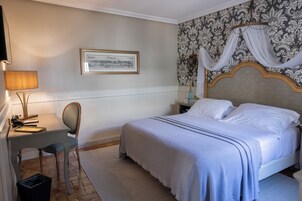 Quarto com cama, escrivaninha, cadeira, quadro na parede e papel de parede estampado.