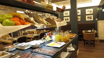A buffet with various breakfast items, including fruits, meats, and beverages.