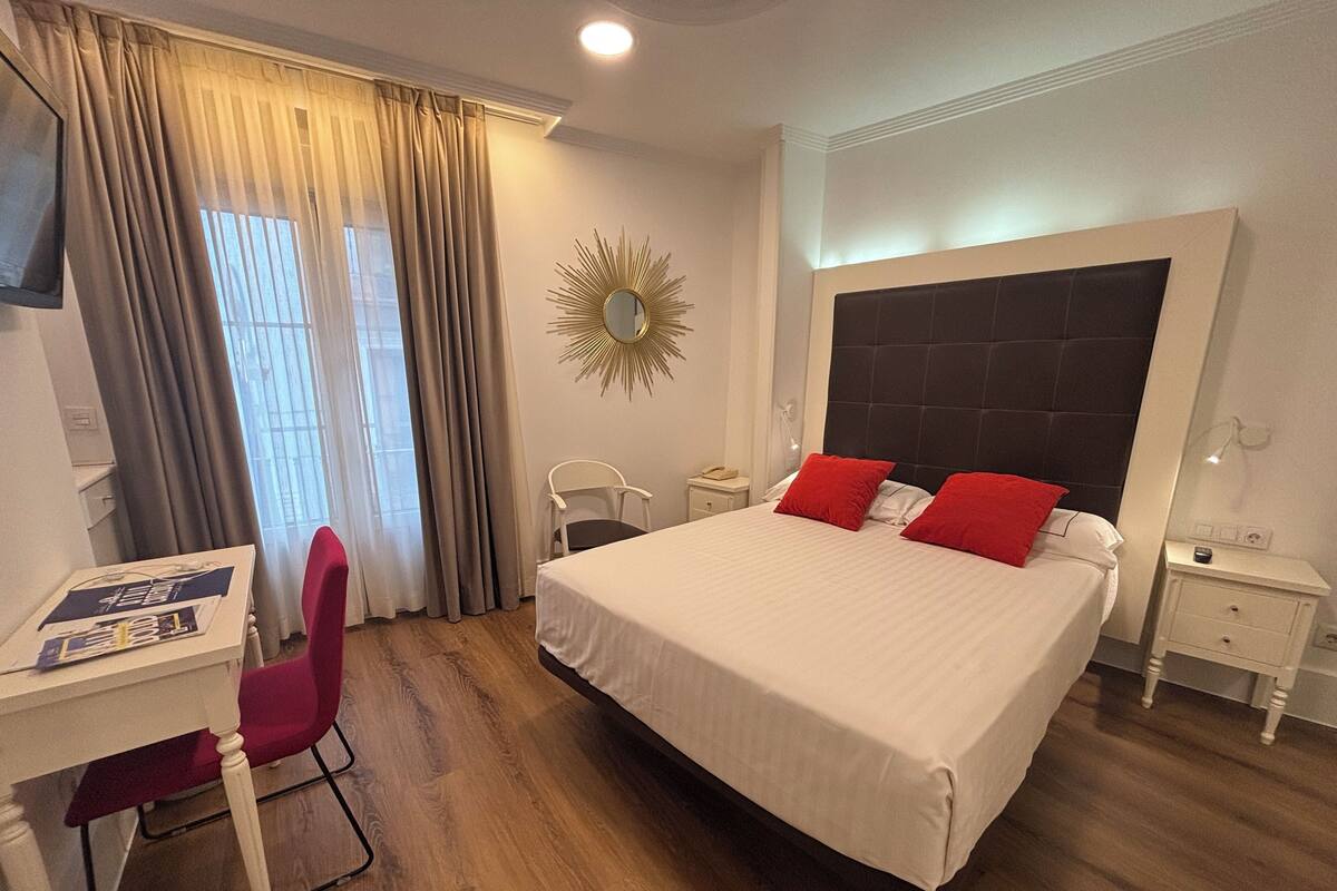 Een hotelkamer met een groot bed, een bureau met stoel, een klein nachtkastje en een spiegel aan de muur.