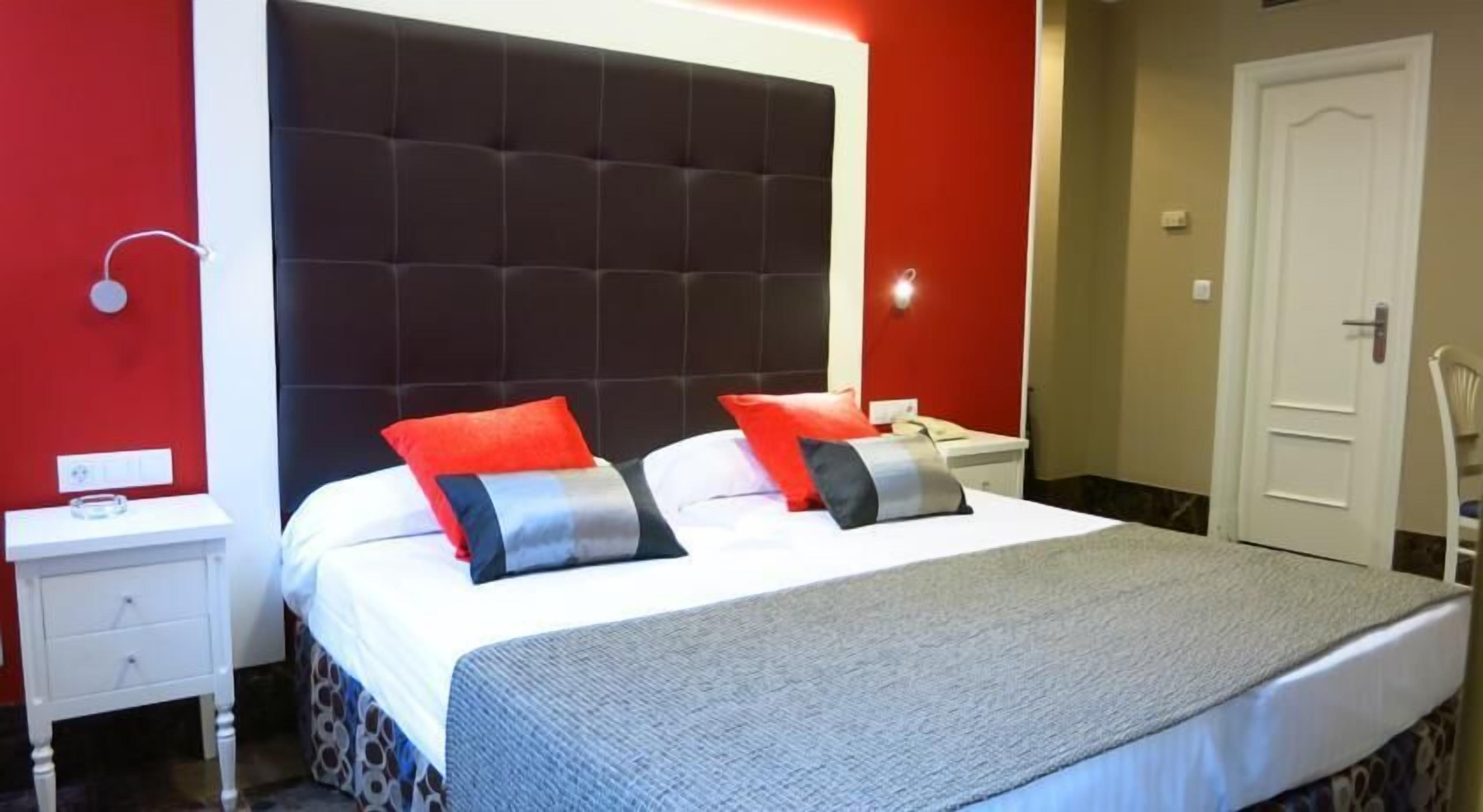 Une chambre d’hôtel avec un grand lit, deux tables de chevet, un mur rouge et une porte.