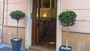 The entrance to Hotel Catedral with a sign above the door, a staircase leading inside, and two potted trees on the sidewalk.