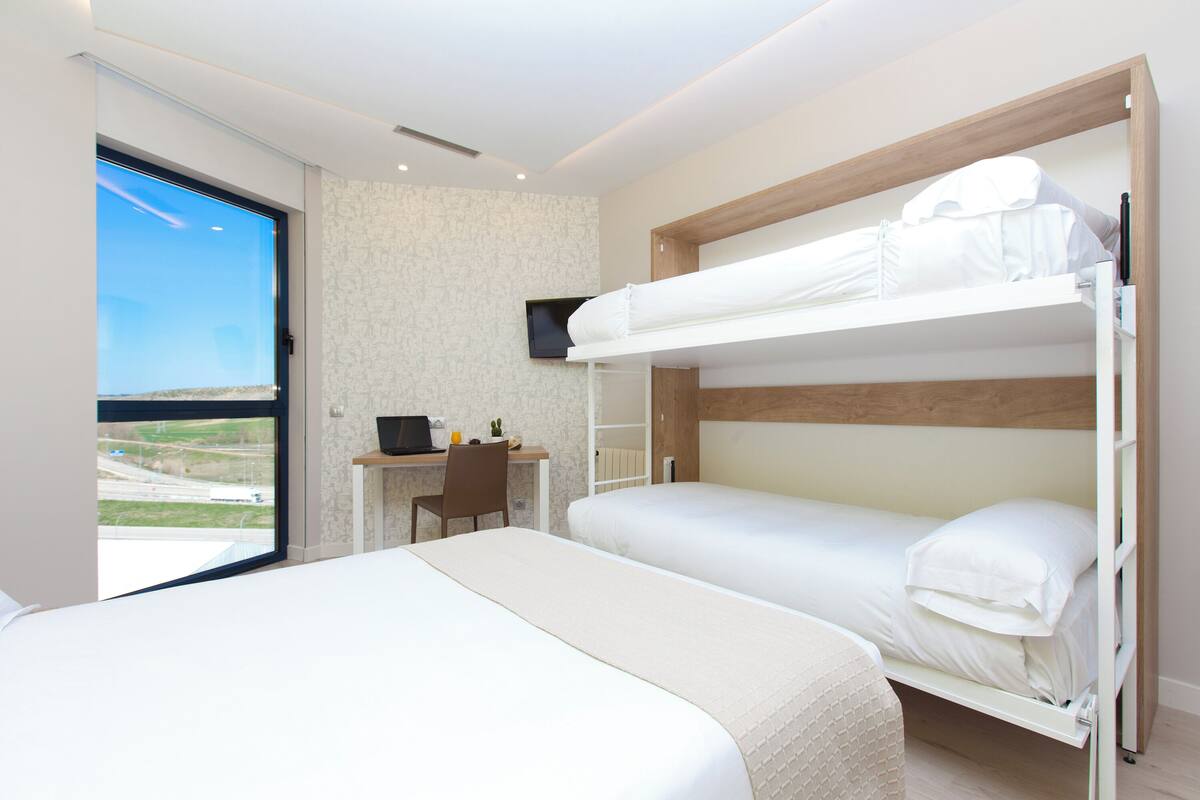 Habitación de hotel con dos camas literas, un escritorio con silla, un televisor y vistas al exterior.