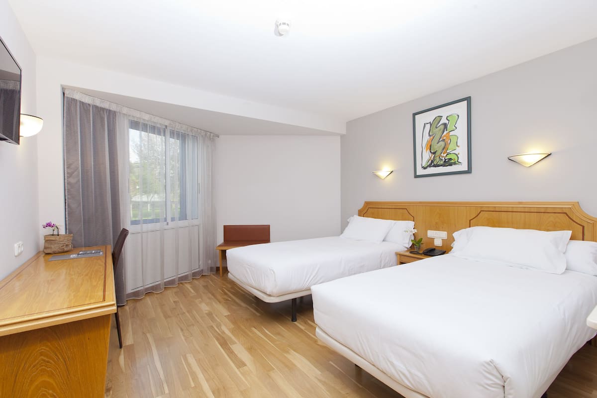 Habitación de hotel con dos camas, un escritorio, una silla y un ventanal con cortinas.