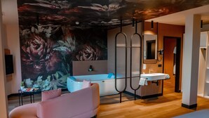Un baño moderno con un gran mural floral, un sofá rosa, una bañera y un lavabo.