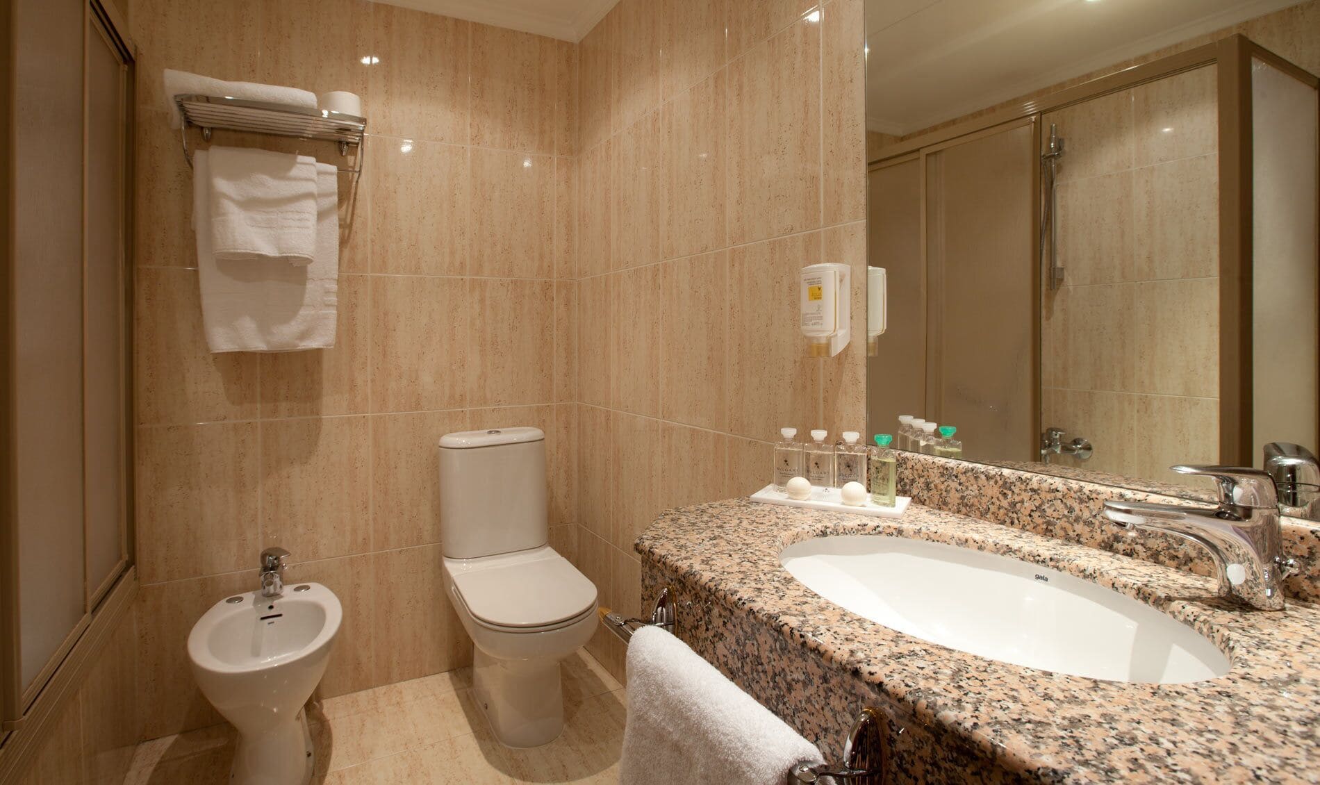 A modern bathroom with a sink, mirror, toilet, bidet, and towel rack.