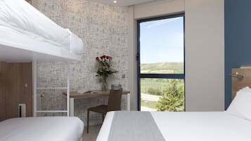 Ett modernt hotellrum med en våningssäng, ett skrivbord med en stol, en vas med blommor och ett stort fönster med utsikt över omgivningarna.