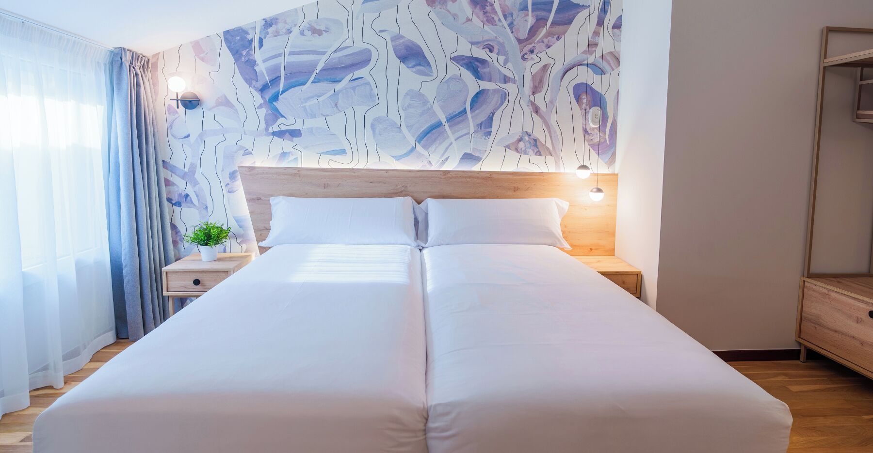 Cama doble con sábanas blancas, cabecera de madera y mesita de noche con una planta.