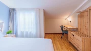 A bedroom with a bed, a desk, a chair, a wardrobe, and a window with curtains.