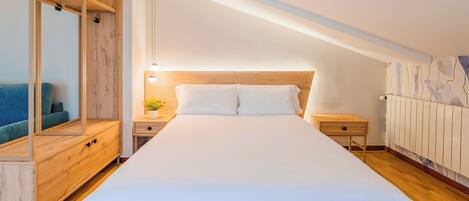 Un dormitorio moderno con una cama grande, cabecera de madera, mesitas de noche, una planta pequeña y un radiador.