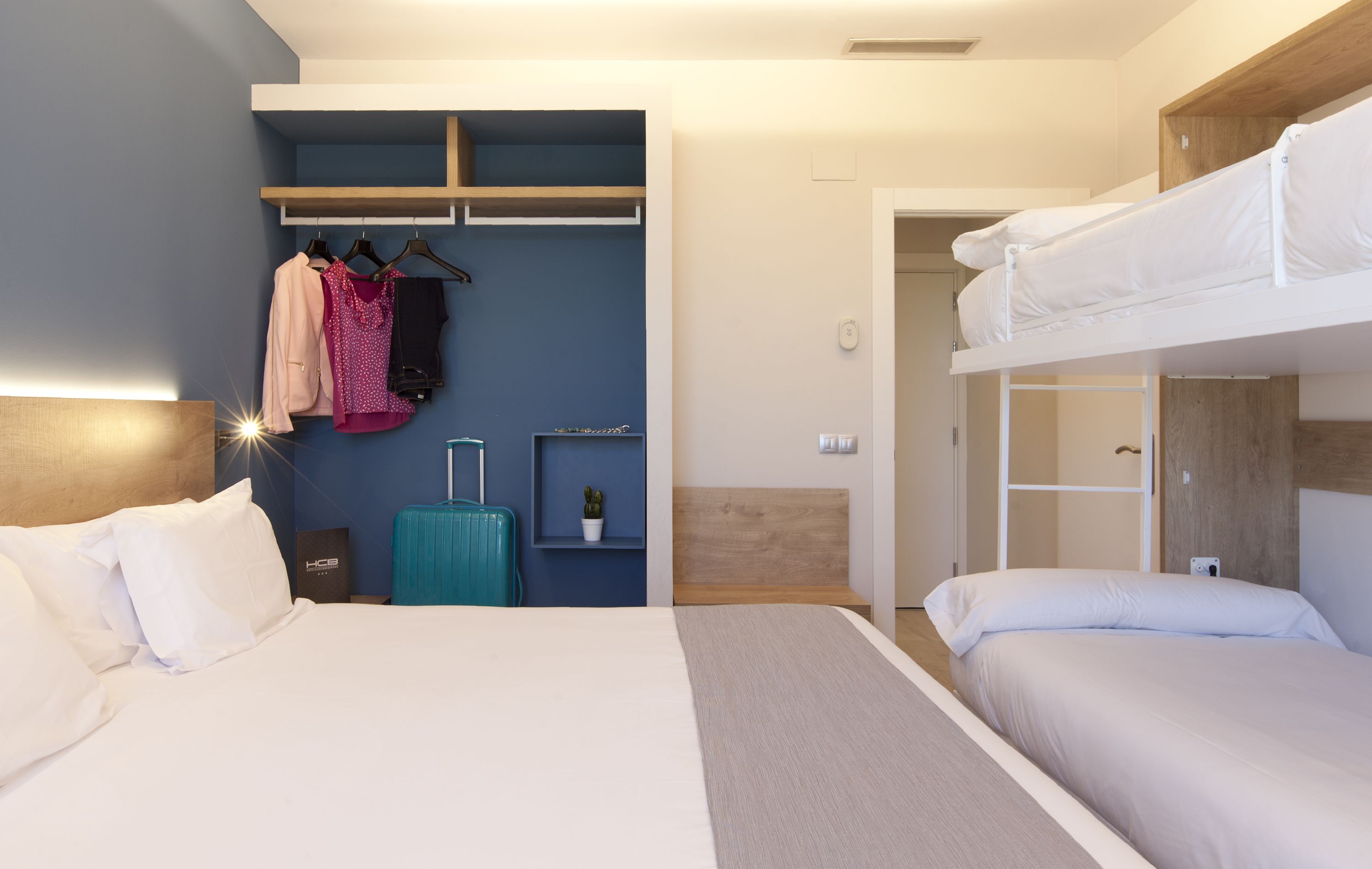 Una habitación de hotel con cama, maleta, armario y literas.