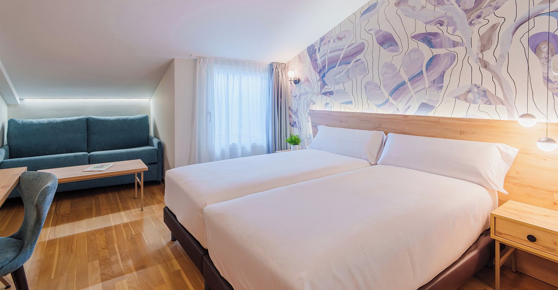 Habitación de hotel con una cama grande, un sofá, una mesita y una pared decorada con arte abstracto.