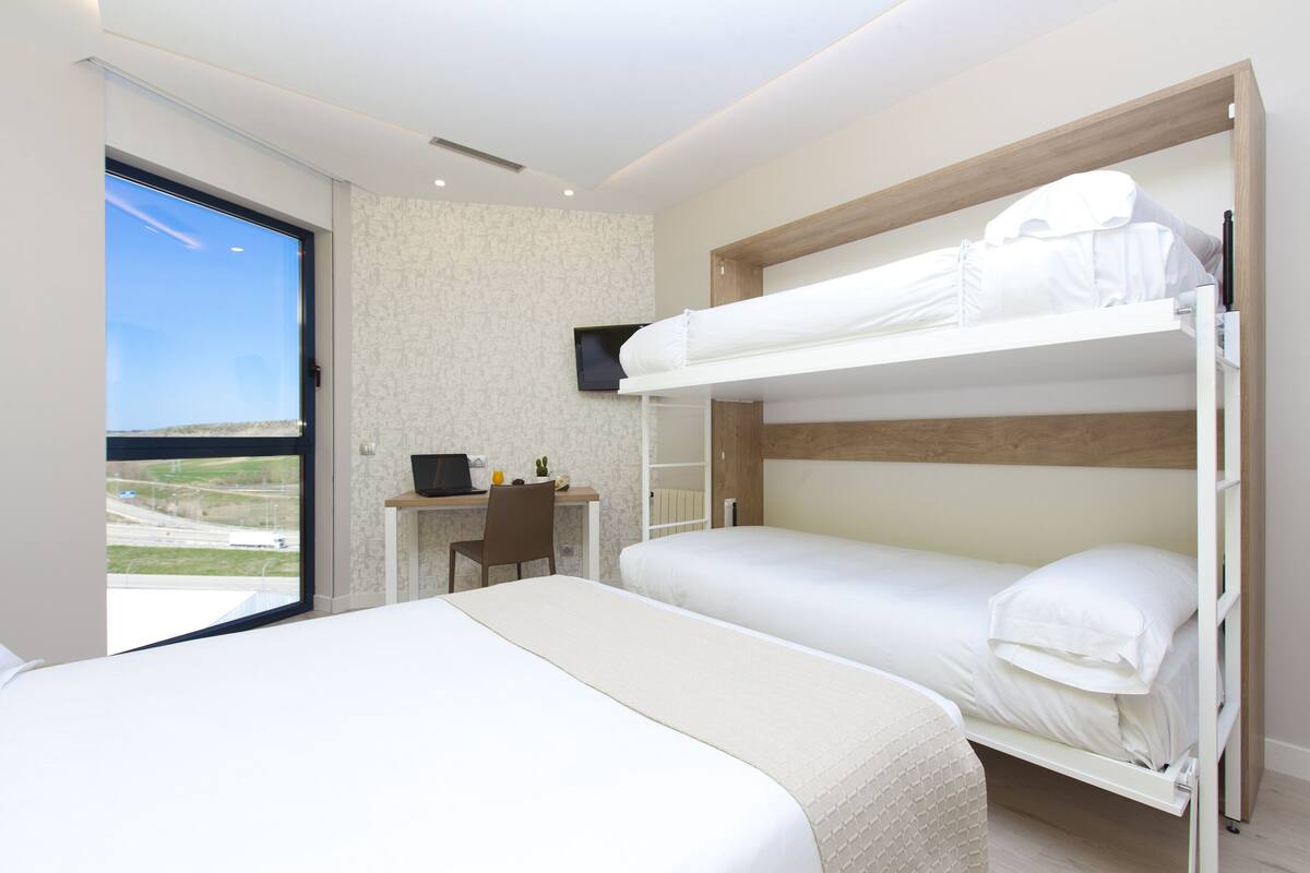 Habitación de hotel con dos camas literas, un escritorio con silla, un televisor y vistas al exterior.
