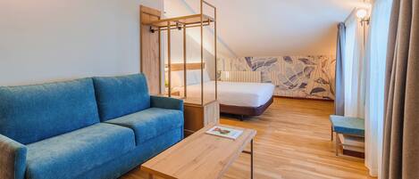 Habitación de hotel moderna con un sofá azul, una mesa de centro de madera, una cama con estructura de madera y una pared estampada.