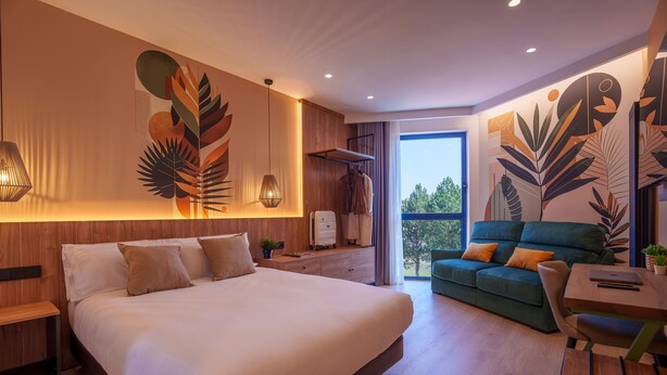 Una habitación de hotel moderna con una cama grande, un sofá, una mesa de comedor y vistas al exterior.