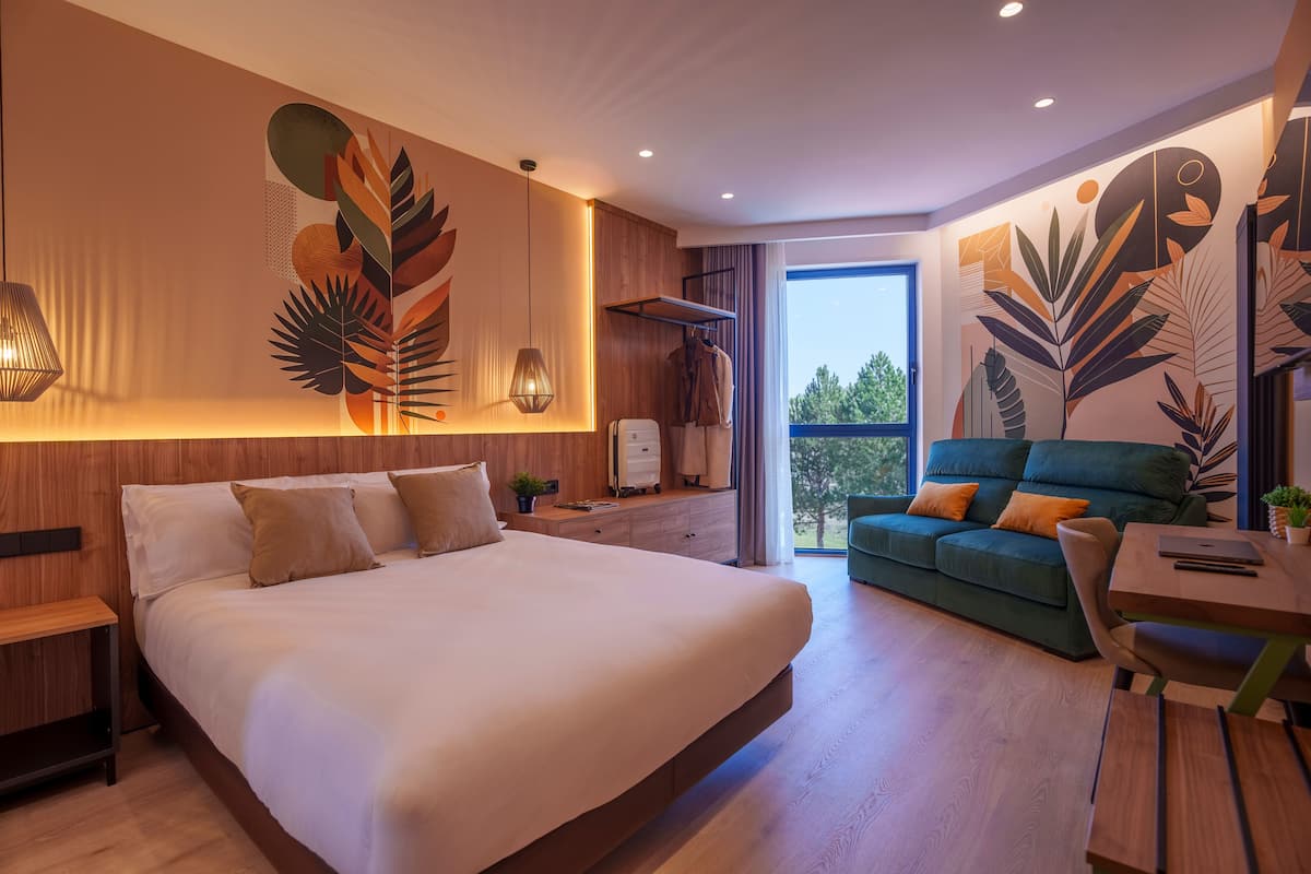 Una habitación de hotel moderna con una cama grande, un sofá, una mesa de comedor y vistas al exterior.