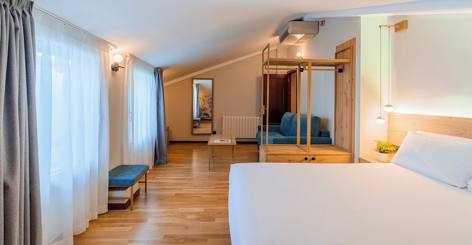 Habitación de hotel con cama, reposabancos, una mesita, un espejo y vistas a un balcón.