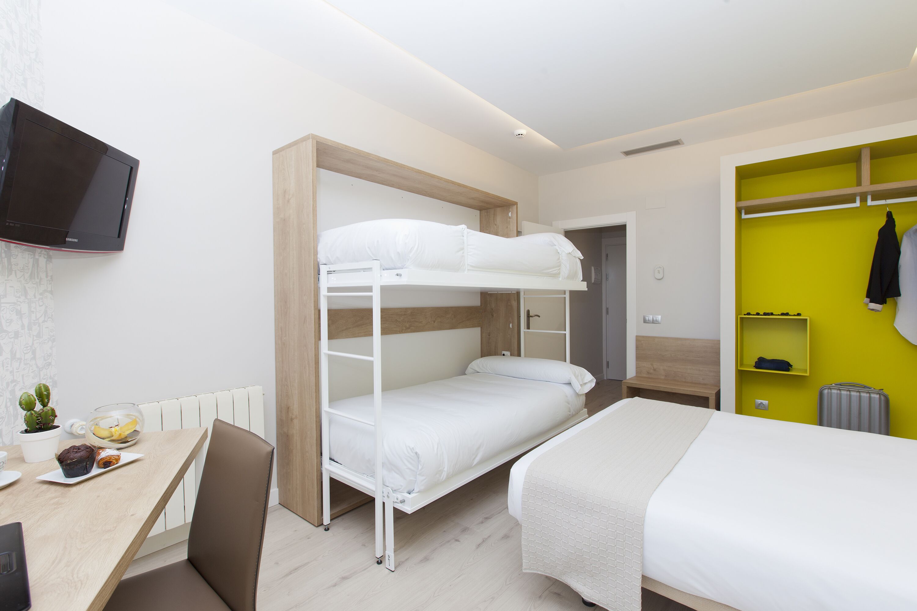 A bunk bed room with a desk, chair, and a TV mounted on the wall.