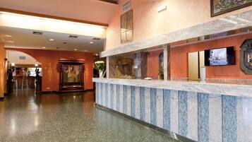 A hotel reception area with a marble counter, a television mounted on the wall, and a framed picture above the counter.