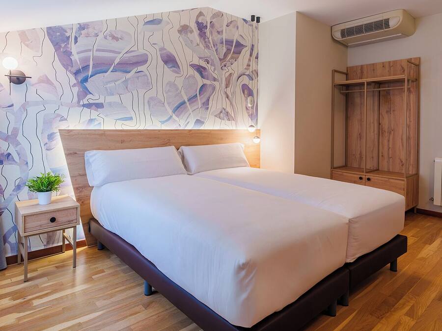 Un dormitorio moderno con cabecera de madera, cama grande, mesita de noche con una planta, armario y radiador.