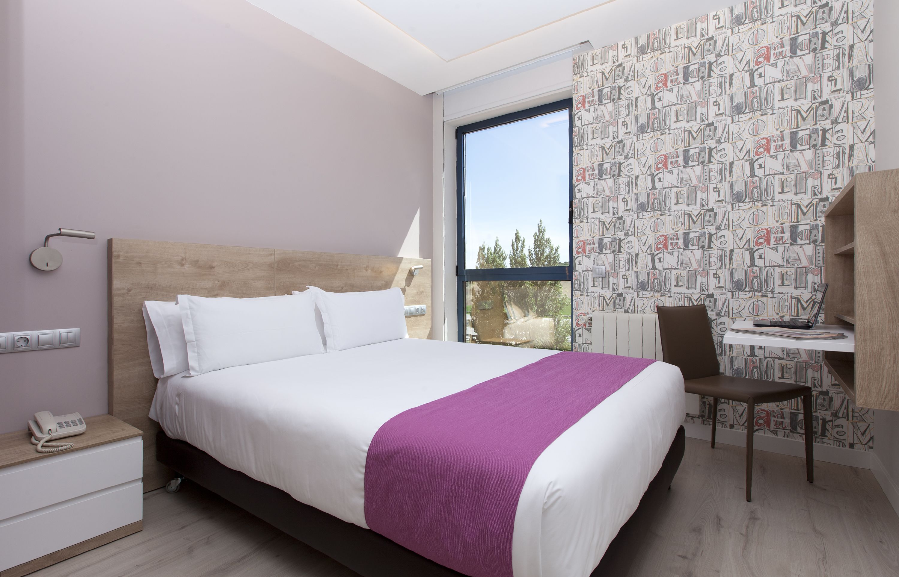 A modern hotel room with a large bed, a desk, and a chair.