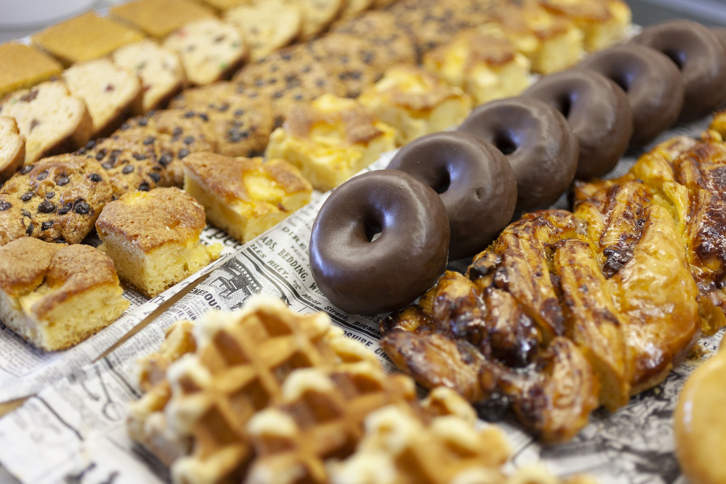Une variété de produits de boulangerie, notamment des biscuits, des gâteaux et des viennoiseries, présentés sur un journal.