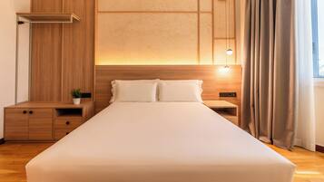 A hotel room with a large bed, wooden nightstands, a bedside table, a wall-mounted shelf, and a window with curtains.