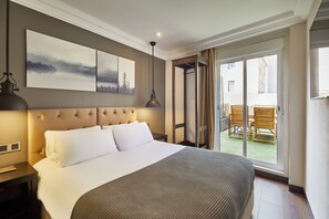 Una habitación de hotel con una cama grande, cabecera, mesita de noche, lámpara y un ventanal corredero que da a un espacio exterior con sillas.