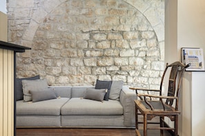 Una habitación con pared de piedra, un sofá gris con cojines y una silla de madera.