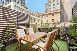 An outdoor patio with a wooden table and chairs, surrounded by planters and a wooden fence. - Hotel Cortes Rambla (Barcelona)