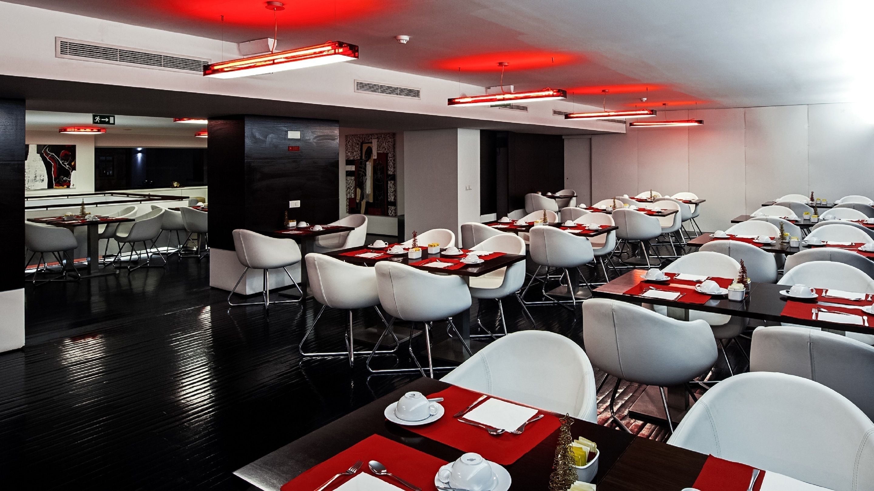 A modern dining area with white chairs and tables, red placemats, and red ceiling lights.