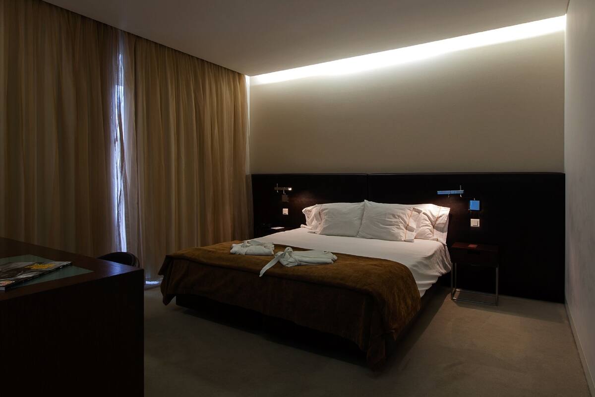 Habitación de hotel con una cama grande, un escritorio con silla y una ventana con cortinas.
