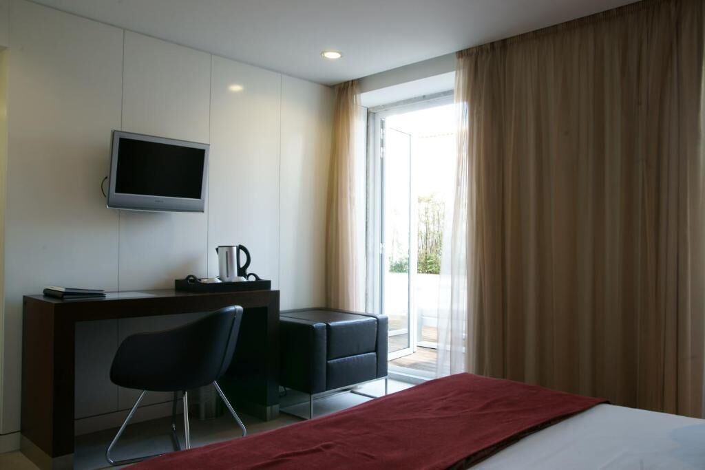Habitación de hotel con cama, escritorio, silla, televisión y ventana con cortinas.