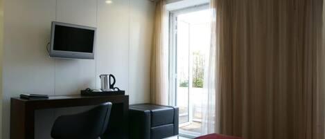 Habitación de hotel con cama, escritorio, silla, televisión y ventana con cortinas.