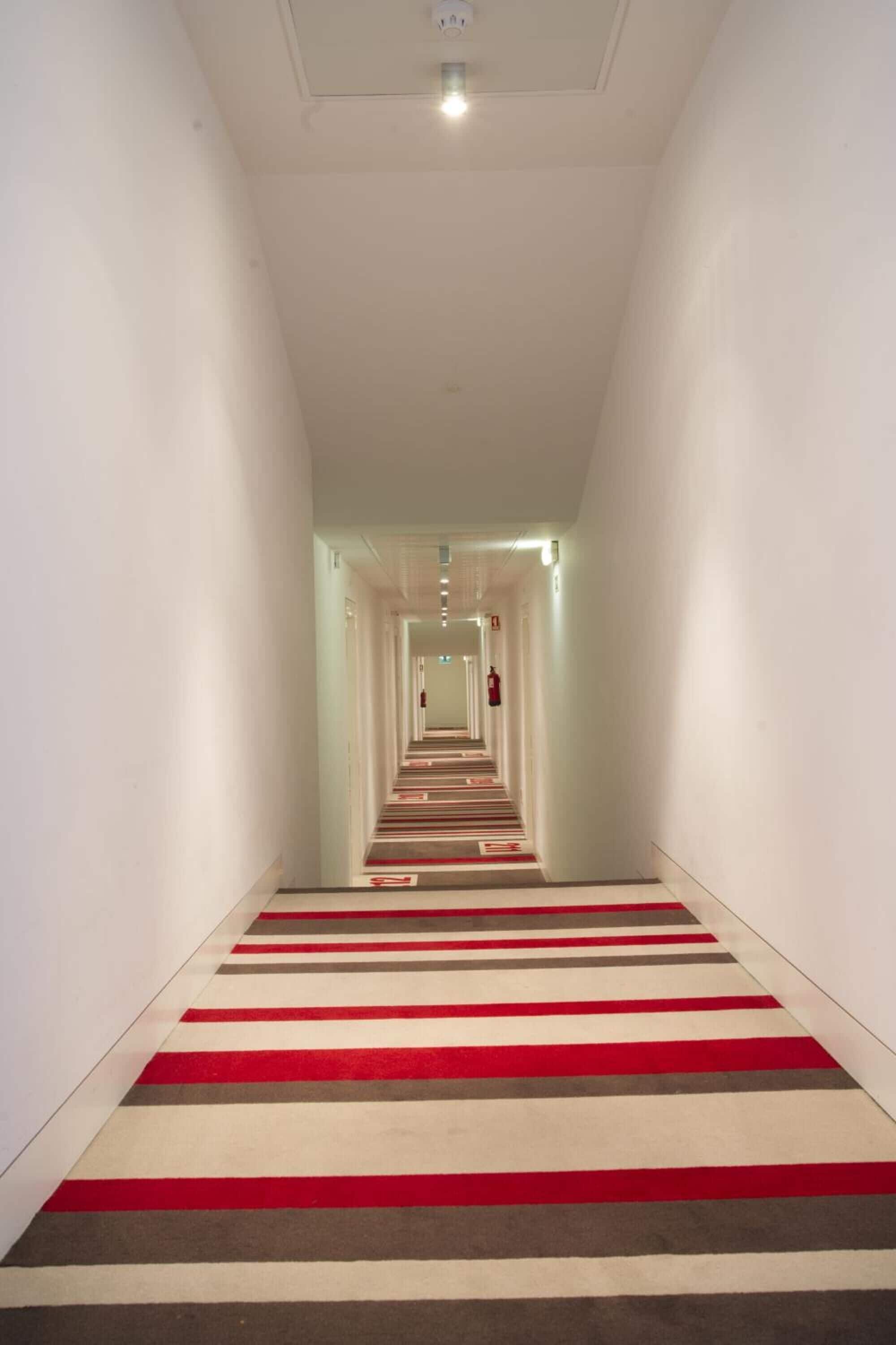 A long, narrow hallway with a striped carpet and a fire extinguisher mounted on the wall.