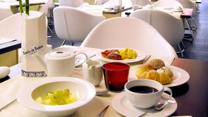 A dining area with white chairs and tables, a bowl of fruit, a coffee cup, and a plate with food. - Hotel Jerónimos 8 (Lisbon)