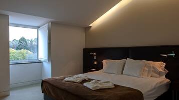 Habitación de hotel moderna con una cama grande, un ventanal con vistas a zonas verdes y un techo curvo.