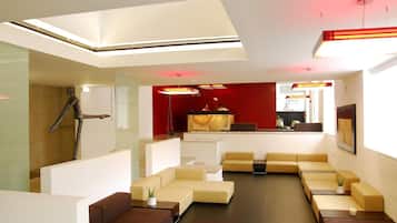 Un moderno vestíbulo de hotel con un mostrador de recepción central, varias áreas de estar y una escalera que sube a un nivel superior.