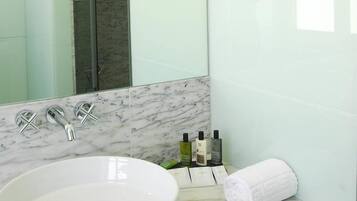 Un baño con un lavamanos blanco, un espejo y una pared con azulejos de mármol.