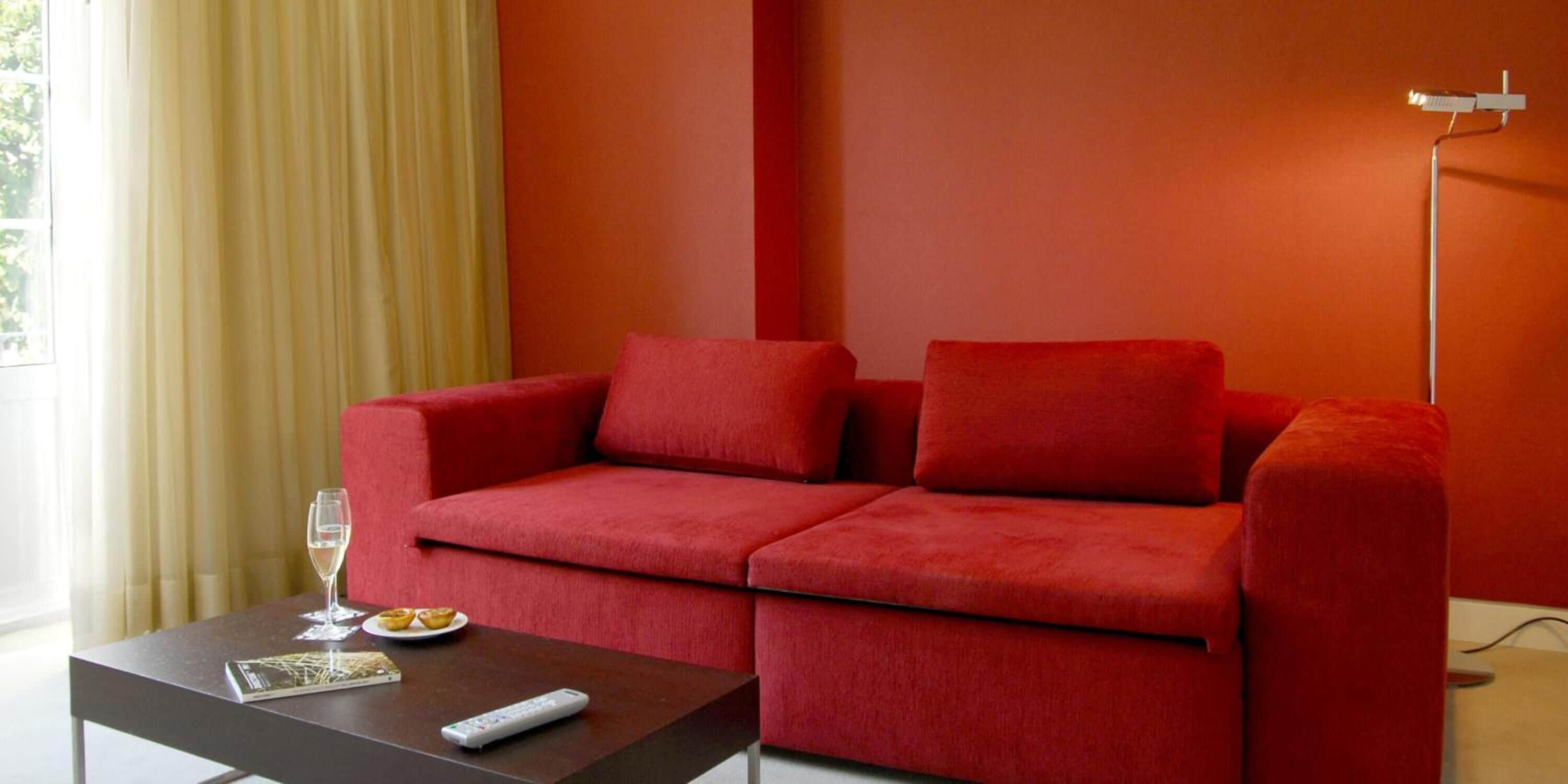 A red sofa with a remote control and a glass of wine on a table.