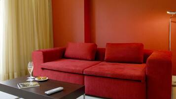 A red sofa with a remote control and a glass of wine on a table.