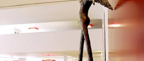 Un interior moderno con una escultura de figura humana sobre un pedestal largo y curvo.